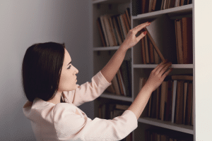 Mulher pegando livros em prateleira de biblioteca em casa.