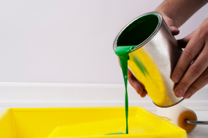 Pessoa derramendo tinta em vasilha para pintar a casa. Processo após entender os diferentes tipos de tintas.
