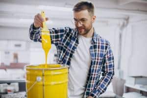 Homem pintando ambiente ao saber como lidar com o cheiro de tinta no ambiente.