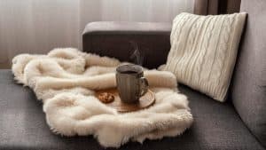 Sofá da sala com manta e almofada seguindo a decoração comfy.