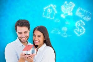 Attractive young couple holding a model house against blue background with vignette